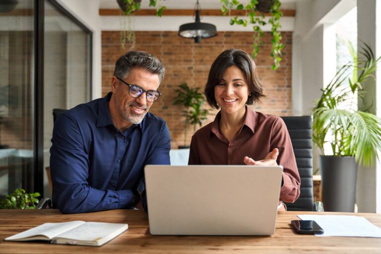 Two colleagues smiling while working together at a laptop