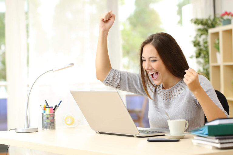 A woman celebrating a win at her laptop